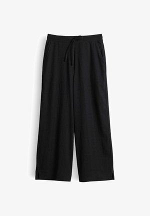 Pantaloni neri a gamba larga con elastico in vita, coulisse, tasche laterali e piccole spacature all'orlo su sfondo bianco.