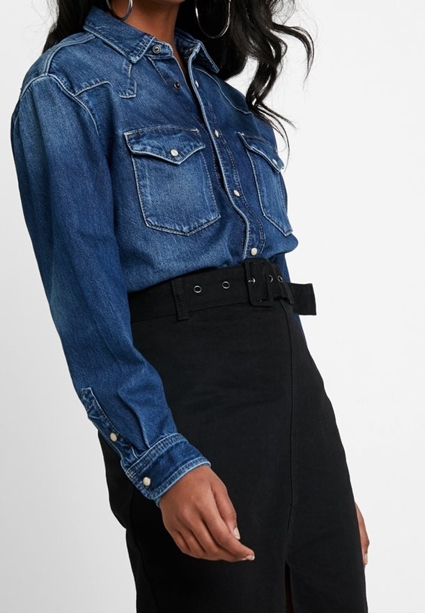 Chemise en denim à boutons, avec deux poches poitrine, boutons-pression et manches longues, assortie d'une jupe noire taille haute avec une ceinture.