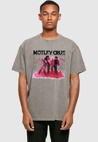 Grå oversized t-shirt med grafiktrykt af tre figurer med pink accenter og sort tekst "MÖTLEY CRÜE." Korte ærmer, rund hals.