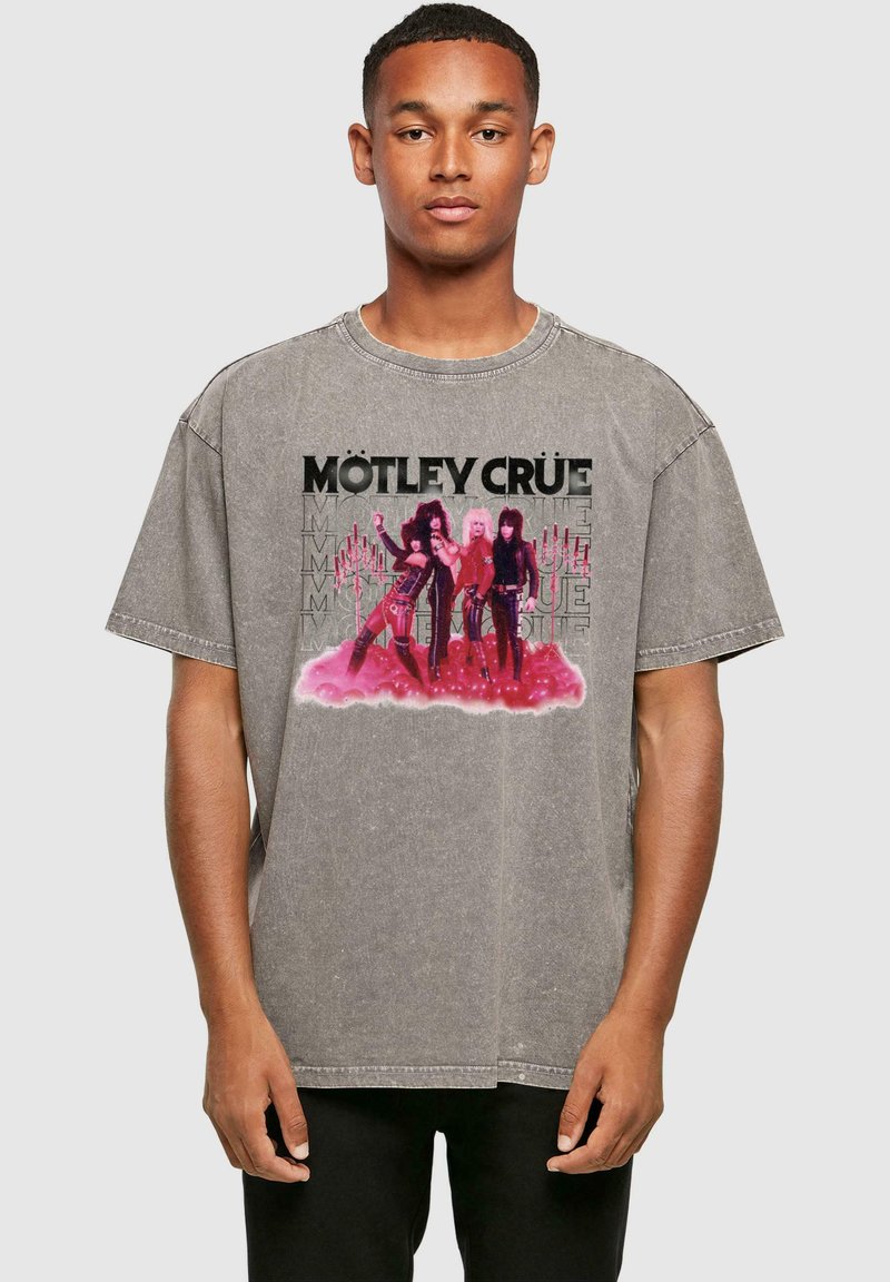 Grå oversized t-shirt med grafiktrykt af tre figurer med pink accenter og sort tekst "MÖTLEY CRÜE." Korte ærmer, rund hals.