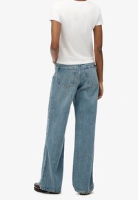 Vaaleansiniset leveälahkeiset farkut, joissa on kaksi takataskua ja hieman haalistunut pinta. Yhdistetty valkoiseen lyhythihaiseen t-paitaan.