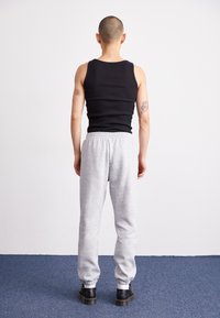 Black ribbed tank top and light gray sweatpants with elastic cuffs, paired with black shoes. Background features a plain white wall and blue carpet.