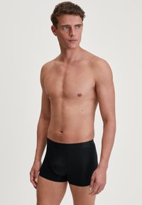 Zwarte boxershorts van een soepel, rekbaar materiaal met een zachte tailleband. Heeft een aansluitend ontwerp met een voorzak voor ondersteuning.