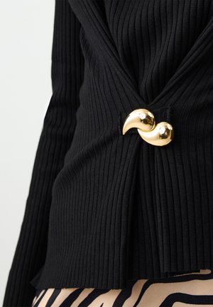 Black ribbed top featuring a twisted design, secured with a shiny gold crescent-shaped clasp at the waist. Textured fabric adds depth.
