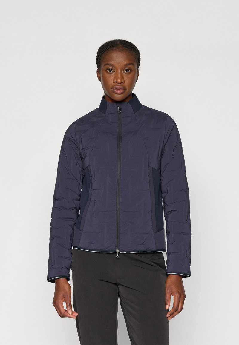 Veste rembourrée marine avec un col haut, fermeture éclair et matériau texturé. Présente des panneaux latéraux élastiques et un empiècement contrastant au niveau des poignets.