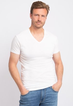 Witte V-hals t-shirt van zachte katoen, met korte mouwen en een slim fit. Draag met blauwe spijkerbroek, handen in de zakken.