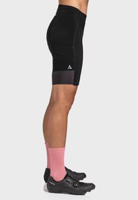 Schwarze Sportshorts mit passgenauer Passform, kontrastierendem schwarzen Band am Saum und kleinem Logo in der Nähe der Seitennaht. Getragen mit rosa Socken und Radschuhen.