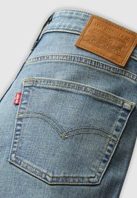 Poche arrière d’un jean Levi’s bleu clair avec coutures jaunes, étiquette rouge Levi’s et étiquette de marque en cuir marron à la taille.