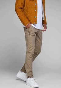 Chinos beiges à coupe slim, associés à un t-shirt blanc et une veste en corduroy moutarde, complétés par des baskets blanches.