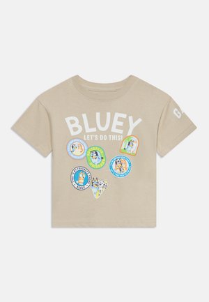 Beige short-sleeve t-shirt with Bluey cartoon characters and text reading "BLUEY LET'S DO THIS!" and various colorful circular patches.