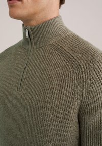 Khaki sweter z wysokim kołnierzem i półzamkiem, z teksturowanym wzorem dzianiny oraz prążkowanymi detalami przy dekolcie i mankietach.