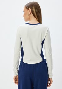 Long-sleeve top with a cream front and navy side panels, made from smooth fabric. Features a rounded hem and a crew neckline.