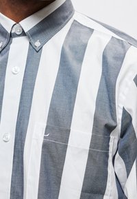 Homme portant une chemise boutonnée avec de larges rayures verticales grises et blanches et un col boutonné.