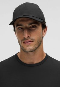 Gorra de béisbol negra con una corona estructurada, tela suave y visera curva, llevada con una camiseta negra de cuello redondo ajustada.