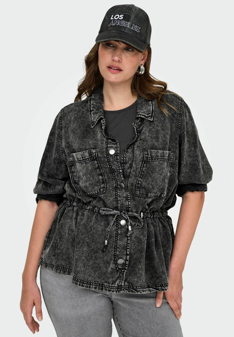 Črna kislo oprana jeans srajca z gumbnim zapiranjem, dvema žepoma na prsih, elastičnim pasom in zavihanimi rokavi, v kombinaciji s črno kapo.