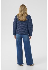 Mornarska puffer jakna s chevron uzorkom, s visokim ovratnikom i dugim rukavima, u kombinaciji s širokim trapericama.