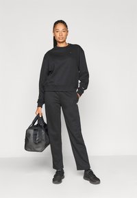 Μαύρο βαμβακερό φούτερ και ταιριαστά παντελόνια φόρμας με ελαστικά μανσέτες, συνοδευόμενα από μαύρη τσάντα duffel. Λείο ύφασμα, άνετη εφαρμογή, ελάχιστη σήμανση.