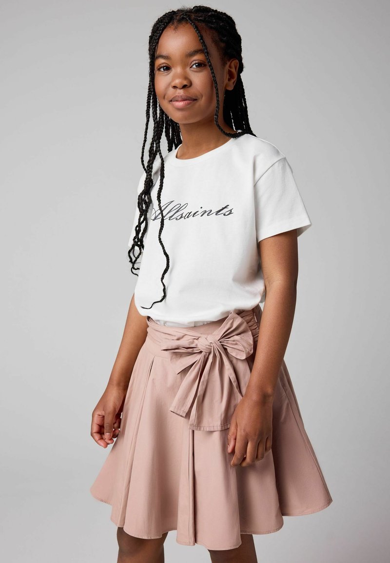 Camiseta blanca con el texto "Allsaints", combinada con una falda rosa pastel que presenta un lazo en la cintura y un diseño plisado.