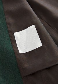 Tissu marron à motifs avec une étiquette blanche rectangulaire cousue à côté d'un tissu texturé vert foncé.