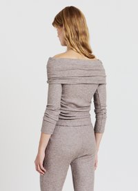 Hellbraunes, geripptes Strick-Oberteil mit weitem Ausschnitt, langen Ärmeln und figurnaher Silhouette, kombiniert mit passenden, gerippten Hosen. Weiche Textur.