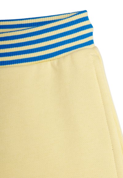 Κίτρινο πλεκτό ύφασμα με ριγέ ελαστική ζώνη στη μέση σε μπλε και κίτρινο, που δείχνει λεπτομέρειες ραφής στο επάνω άκρο του ρούχου.