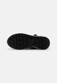 Semelle de chaussure en caoutchouc noir avec un motif texturé, comportant une forme de losange en relief pour l'adhérence. Design épuré avec des accents minimaux.