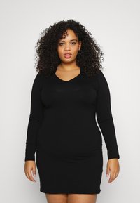 Vestido preto de mangas longas com design em V. Feito de um tecido suave e elástico. Silhueta justa, com a barra acima dos joelhos.