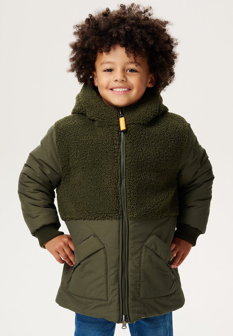 Doudoune verte avec une partie supérieure en texture moelleuse, capuche surdimensionnée et poches latérales. Comprend une fermeture éclair à l'avant et des poignets côtelés.