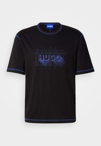 T-shirt de algodão preta com mangas curtas, costura azul e um logótipo gráfico "HUGO" em vários tons de azul na frente.