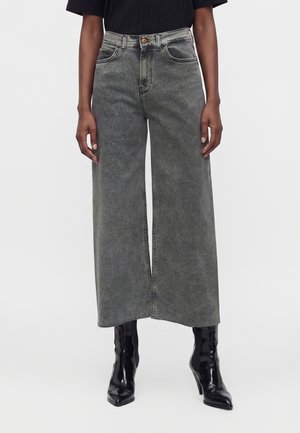 Personne portant un jean large délavé gris taille haute raccourci au-dessus de bottes noires à talons pointus.