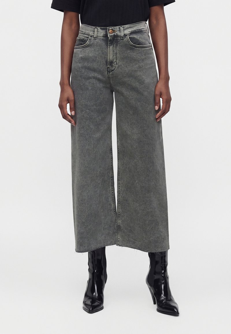Personne portant un jean large délavé gris taille haute raccourci au-dessus de bottes noires à talons pointus.