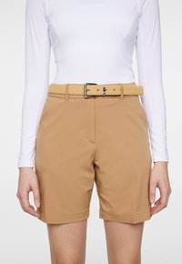 Ljusbruna shorts i smidigt tyg, med en bred midjeresår och ett ljusfärgat bälte med en silverfärgad spänne. Synliga sidofickor.