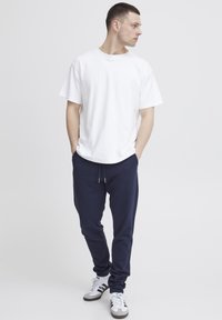 Witte katoenen t-shirt met een ronde hals, gecombineerd met marineblauwe joggingsbroek met een elastische tailleband. Draagt witte en grijze sneakers.