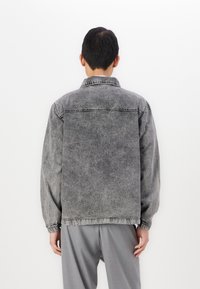 Gray denim jacket with a faded appearance, classic collar, and elastic cuffs. Features stitching along the shoulder and back seam.