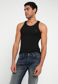 Μαύρο βαμβακερό τοπ χωρίς μανίκια με στρογγυλή λαιμόκοψη, σε συνδυασμό με σκούρο τζιν παντελόνι με διακριτική ξεθώριαση και κούμπωμα με κουμπί.