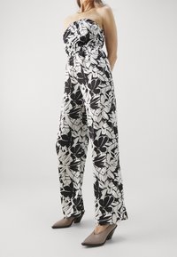 Mono floral en blanco y negro con un corpiño elástico sin tirantes y pantalones de pierna ancha, combinado con tacones de punta beige.