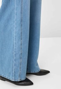 Jeans in denim azzurro chiaro a gamba larga con orlo grezzo e cuciture a contrasto, abbinati a ballerine nere in pelle con punta appuntita.