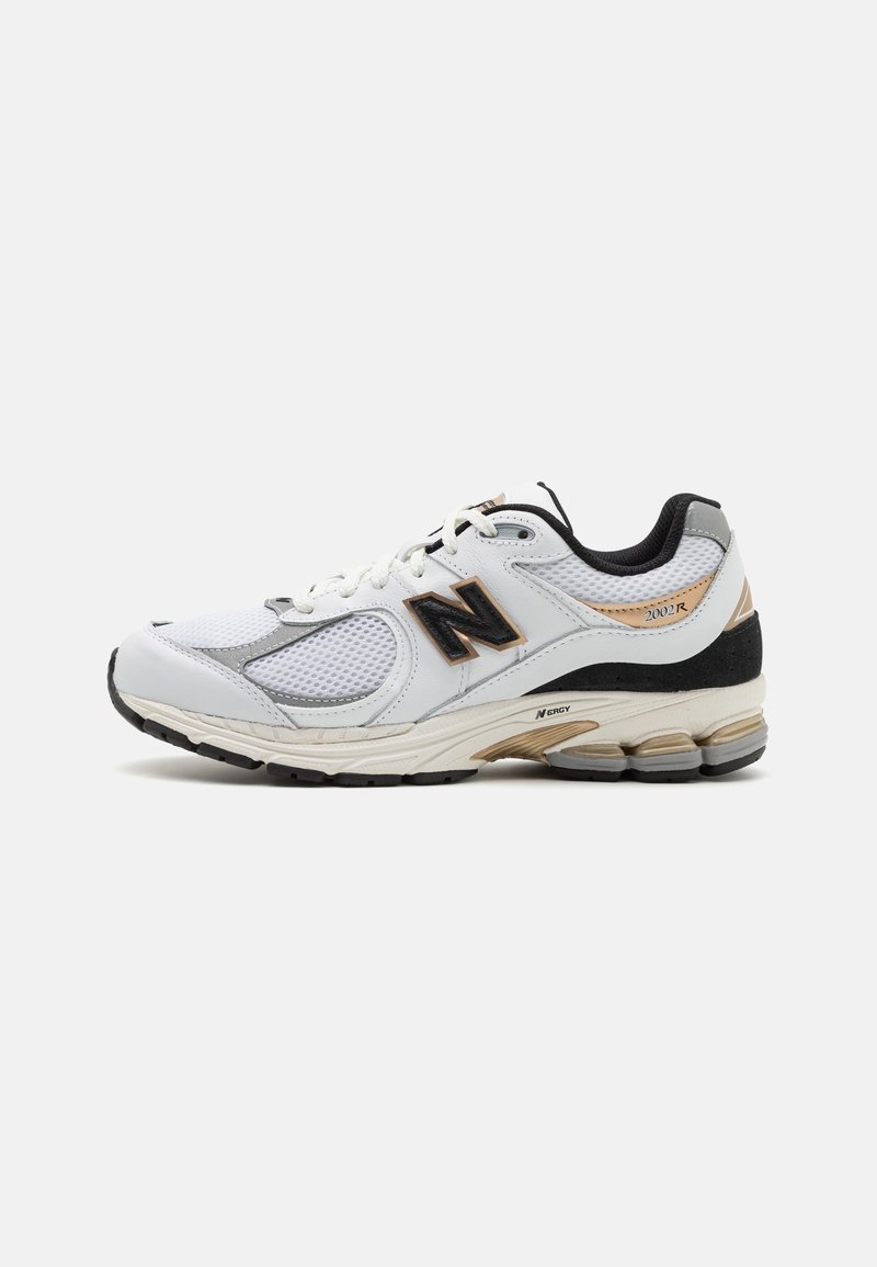 Chaussure de sport blanche avec tige en mesh et synthétique, dotée d'accents noirs et dorés, surface texturée, semelle rembourrée et forme arrondie de l'avant-pied.