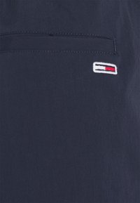 Tissu bleu marine présentant une texture subtile et un petit logo brodé avec des accents rouges, blancs et bleus sur le côté gauche.