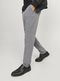 Pantalons gris évasés avec une texture lisse et des poches latérales, associés à des chaussures en cuir noires avec un bout arrondi et des lacets.