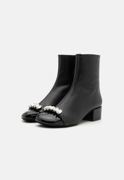 Black leather ankle boots with a glossy toe cap and crystal-accented straps. Square block heel, smooth texture, tight fit. Notable sheen.