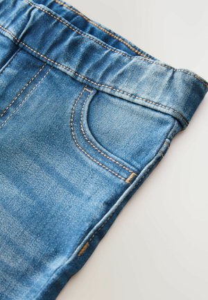 Jeanși din denim cu o spălare albastră deschisă, având un tiv elastic, cusături decorative și un singur buzunar aplicat pe spate.