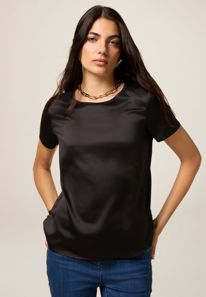 Top corto nero a maniche corte in tessuto morbido con scollatura rotonda e vestibilità rilassata. Abbinato a jeans blu con una leggera lucentezza.
