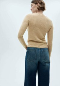 Beige knitted sweater with long sleeves, fitted at the waist. Paired with high-waisted dark blue jeans featuring back pockets.