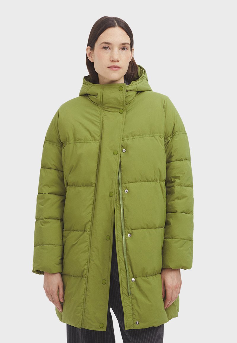 Cappotto puffer verde con cappuccio, caratterizzato da una superficie testurizzata, chiusure a scatto e una lunghezza fino al ginocchio. Il tessuto appare leggero e isolato.