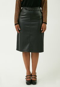 Schwarzer Leder-Bleistiftrock mit taillierter Taille, glatter Textur und geradem Schnitt, kombiniert mit schwarzen Plattformschuhen mit dekorativen Riemen.
