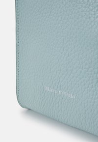 Superficie in pelle testurizzata di colore azzurro chiaro con "Marc O'Polo" impresso in piccole lettere bianche vicino a un bordo cucito.
