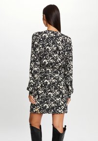 Robe à motif abstrait noir et beige, manches longues, taille cintrée et ourlet légèrement évasé, en tissu léger.