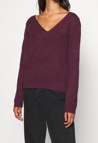 V-ringad långärmad tröja i djup plommonfärg. Texturerat stickningsmönster med avslappnad passform, ribbad nederkant och ärmmuddar, kompletterad av en minimalistisk design.