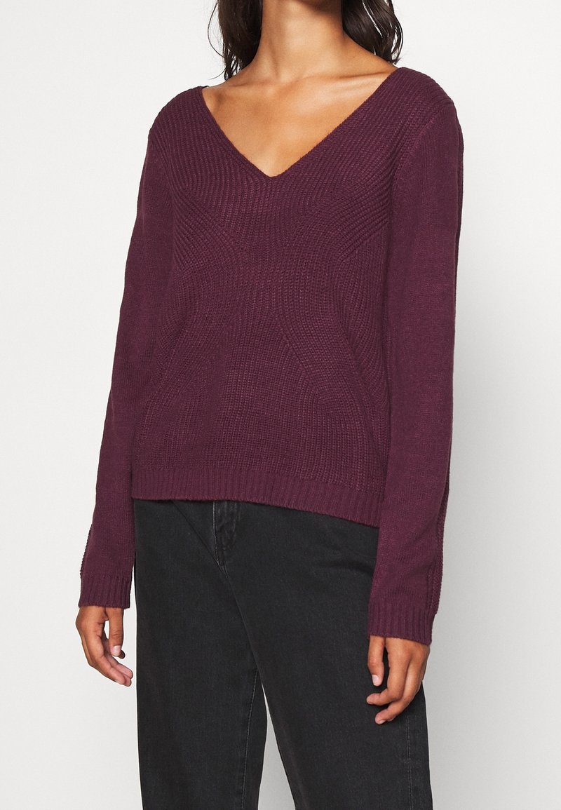 V-ringad långärmad tröja i djup plommonfärg. Texturerat stickningsmönster med avslappnad passform, ribbad nederkant och ärmmuddar, kompletterad av en minimalistisk design.